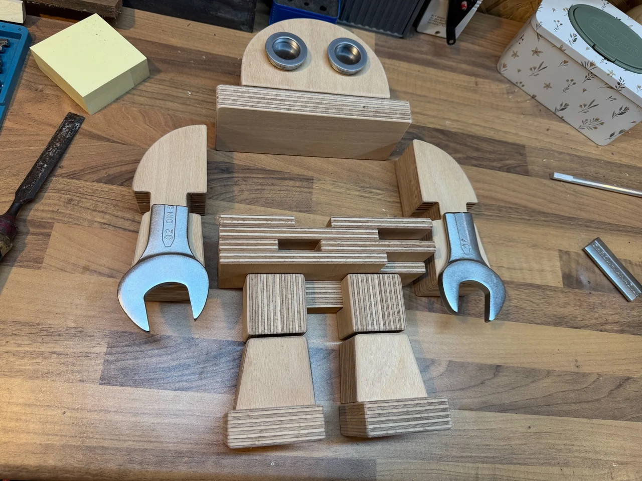 Holzteile und Schraubenschlüssel für die Makey-Figur, auf einer Werkbank zur Roboterform angeordnet